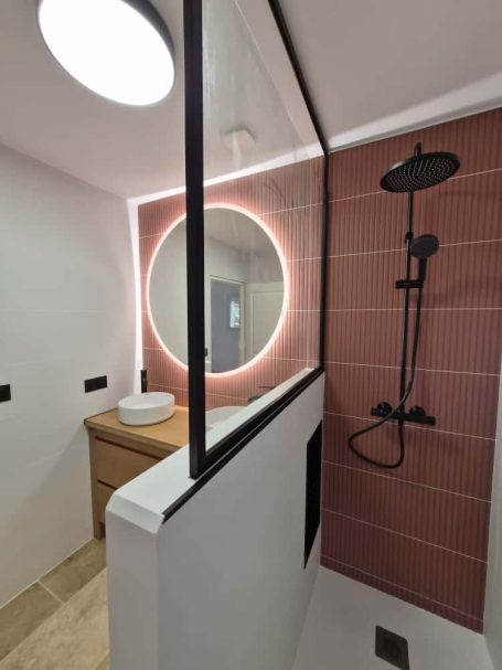 Salle de bain moderne avec douche, miroir rond lumineux et carreaux marron.
